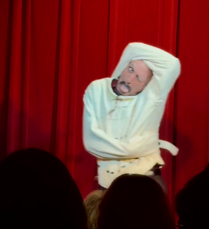 Mid escape, the straitjacket sleeve pulled up over his head as he works an arm loose.