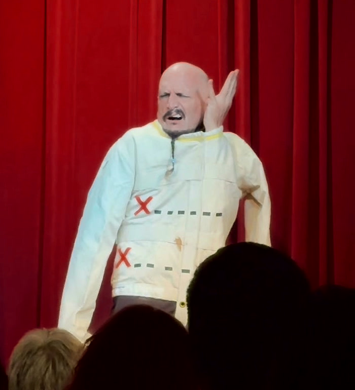 One arm free and raised, jacket hanging open, mid shout to the audience.