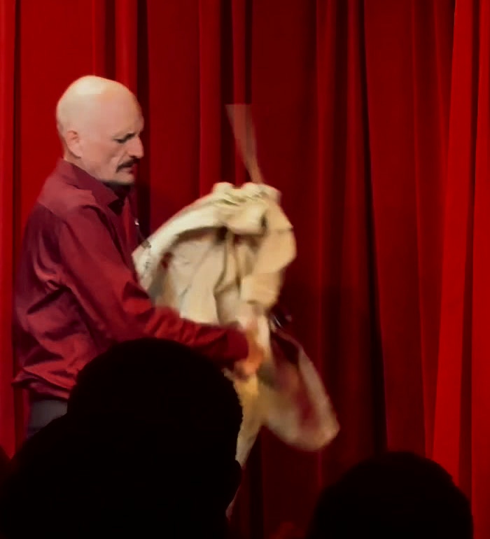Out of it, holding the empty straitjacket up in one hand.